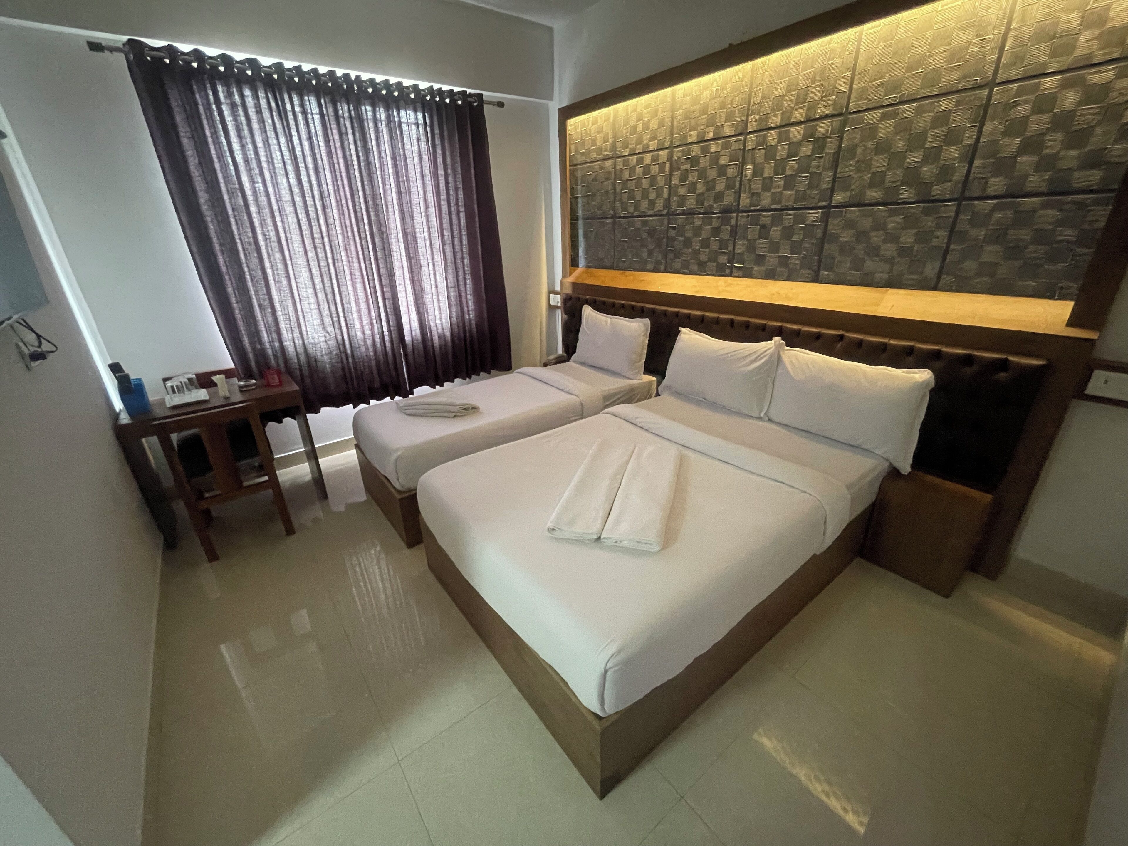 A hotel room with a large bed, two bedside tables, a desk, and a window with curtains.