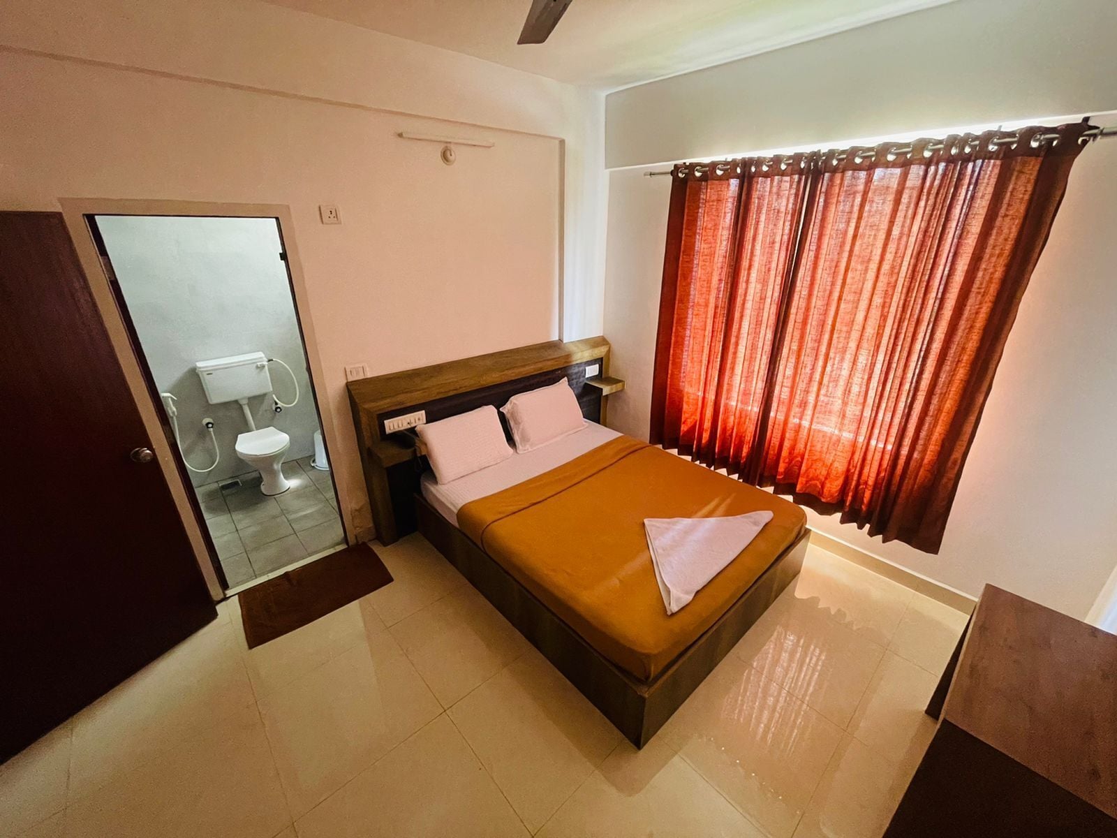 A hotel room with a bed, a bedside table, a mirror, and a window with curtains.