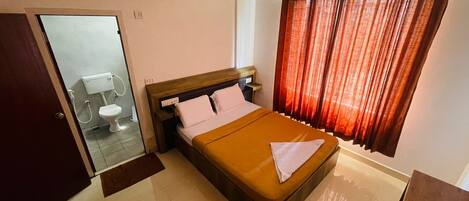 A hotel room with a bed, a bedside table, a mirror, and a window with curtains.