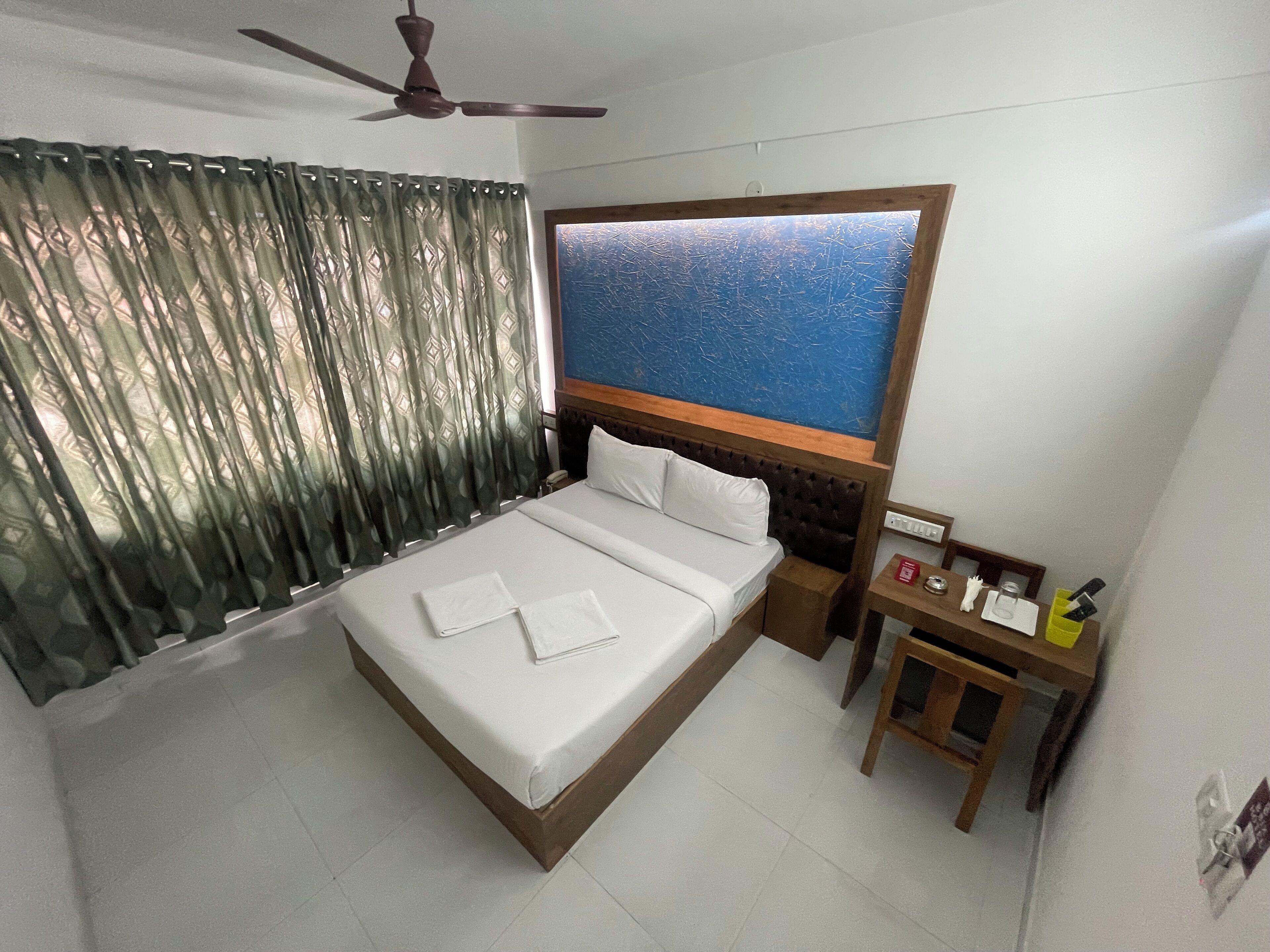 A hotel room with a bed, a wooden headboard, a nightstand, a ceiling fan, and a window with curtains.