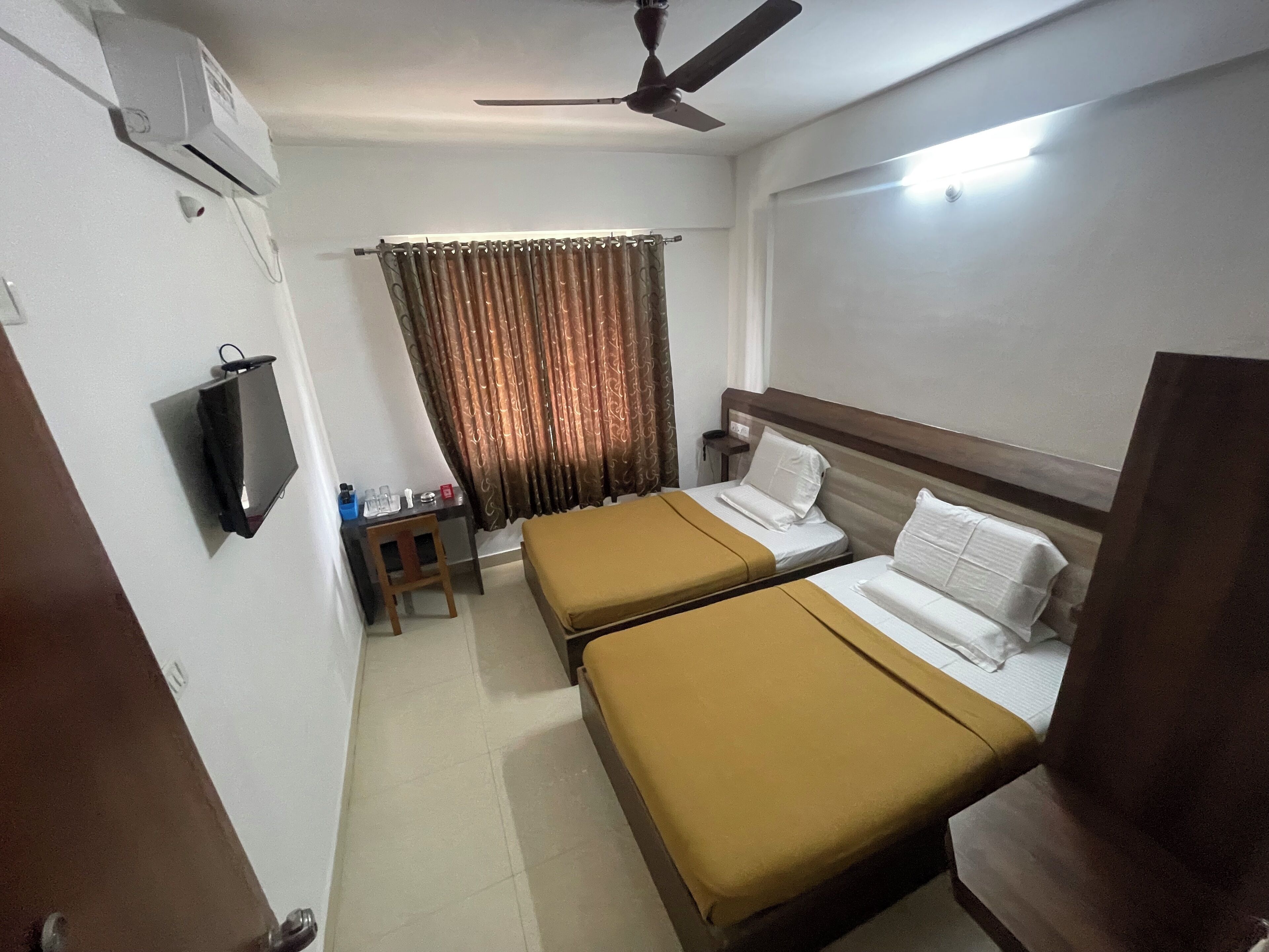 Habitación de hotel con dos camas, un escritorio, una silla, un televisor y un ventilador de techo.