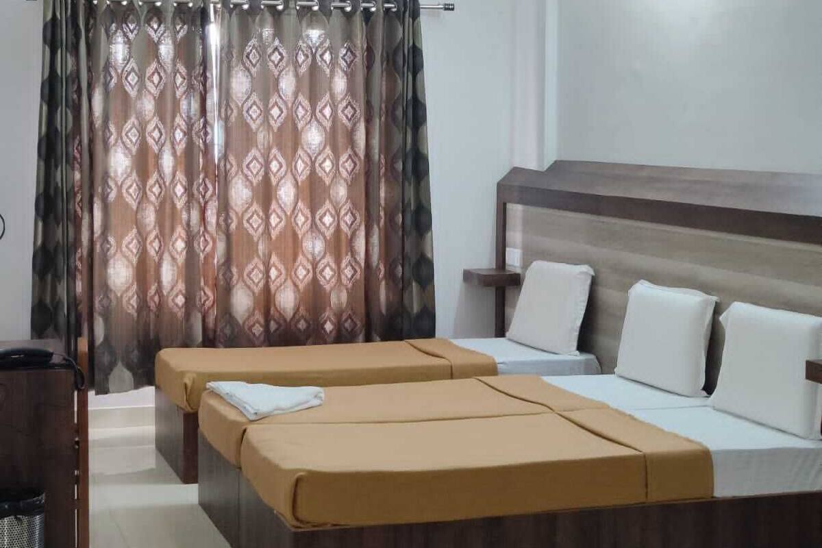 A hotel room with a large bed, a smaller bed, a ceiling fan, and a window with patterned curtains.