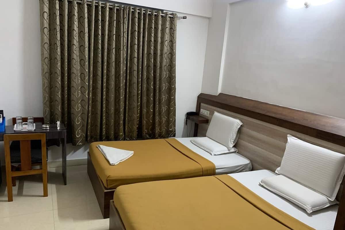 A hotel room with two beds, a wooden headboard, a desk with a chair, and a curtain with a pattern.