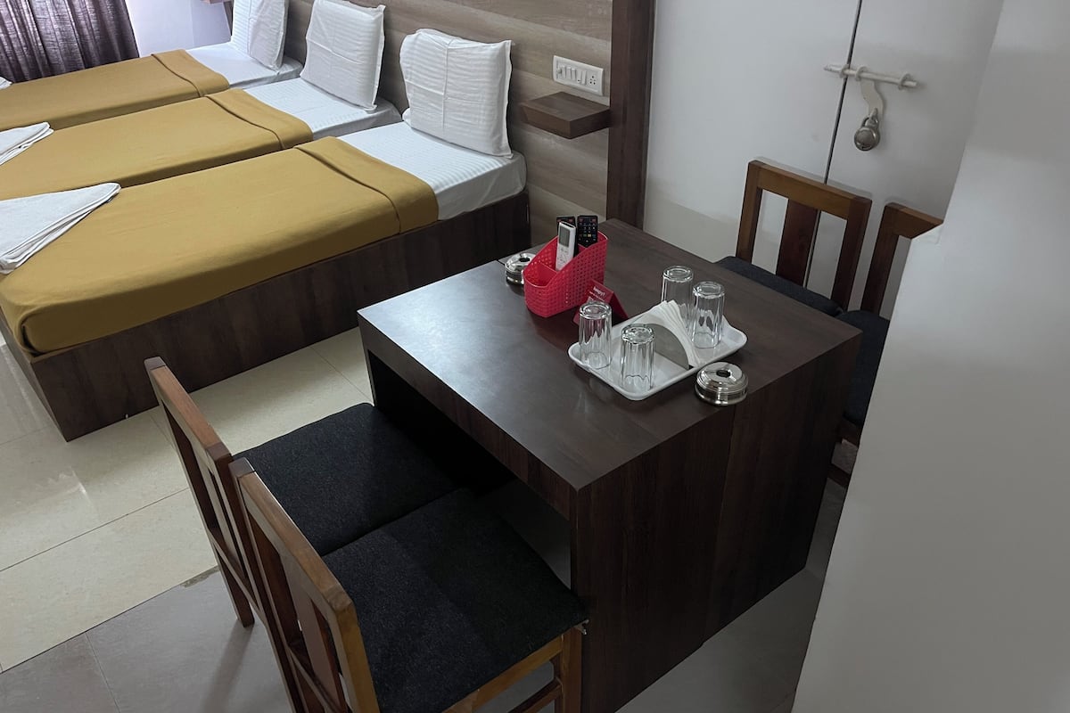 A hotel room with two single beds, a wooden table with a tray of glasses and a red basket, and a wooden chair with a dark cushion.