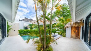 A pool area with a thatched roof, palm trees, and a wooden door. - Villa Mellow (Canggu)