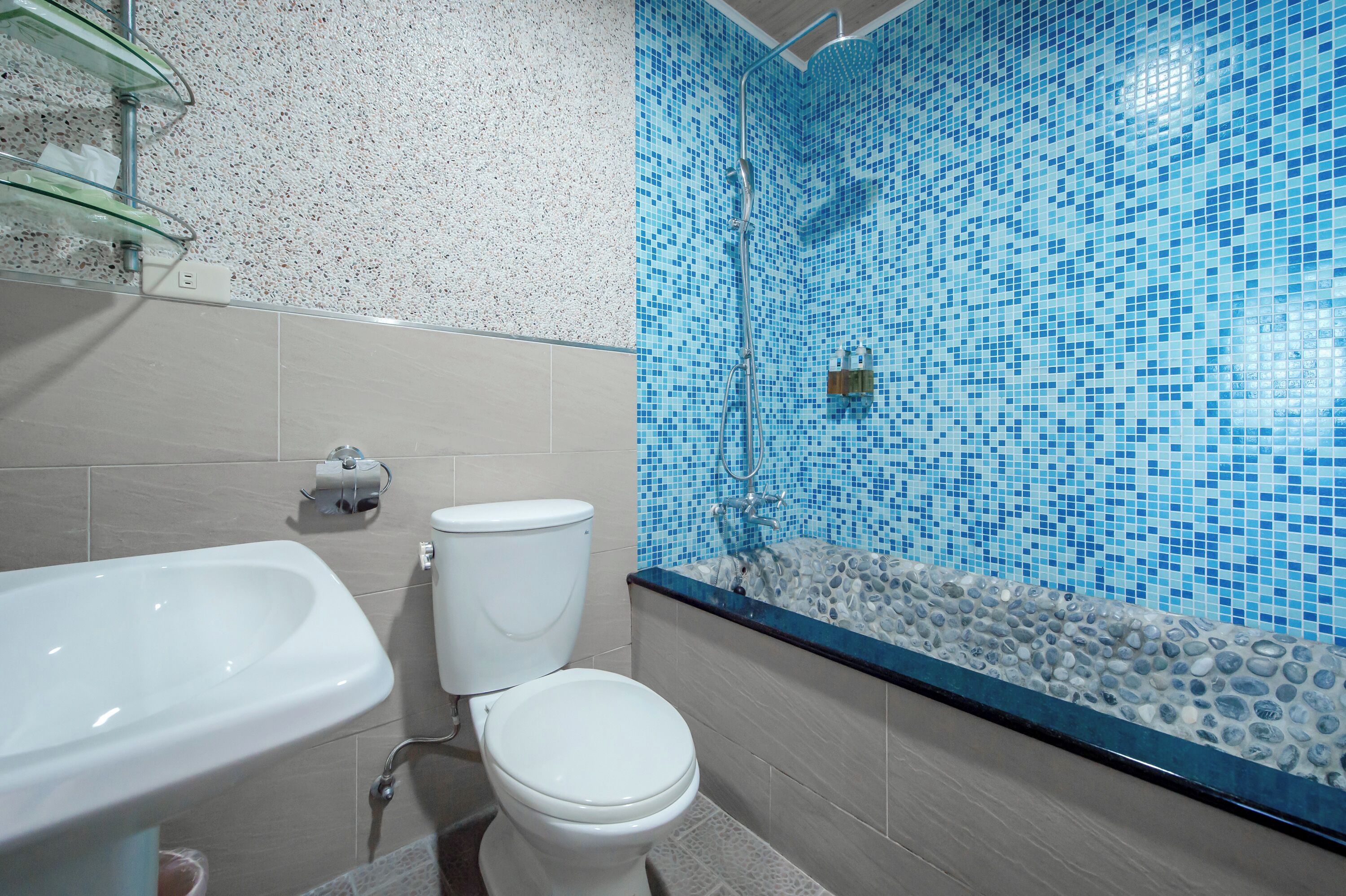 A bathroom with a white sink, toilet, and a shower with a mosaic tile wall.