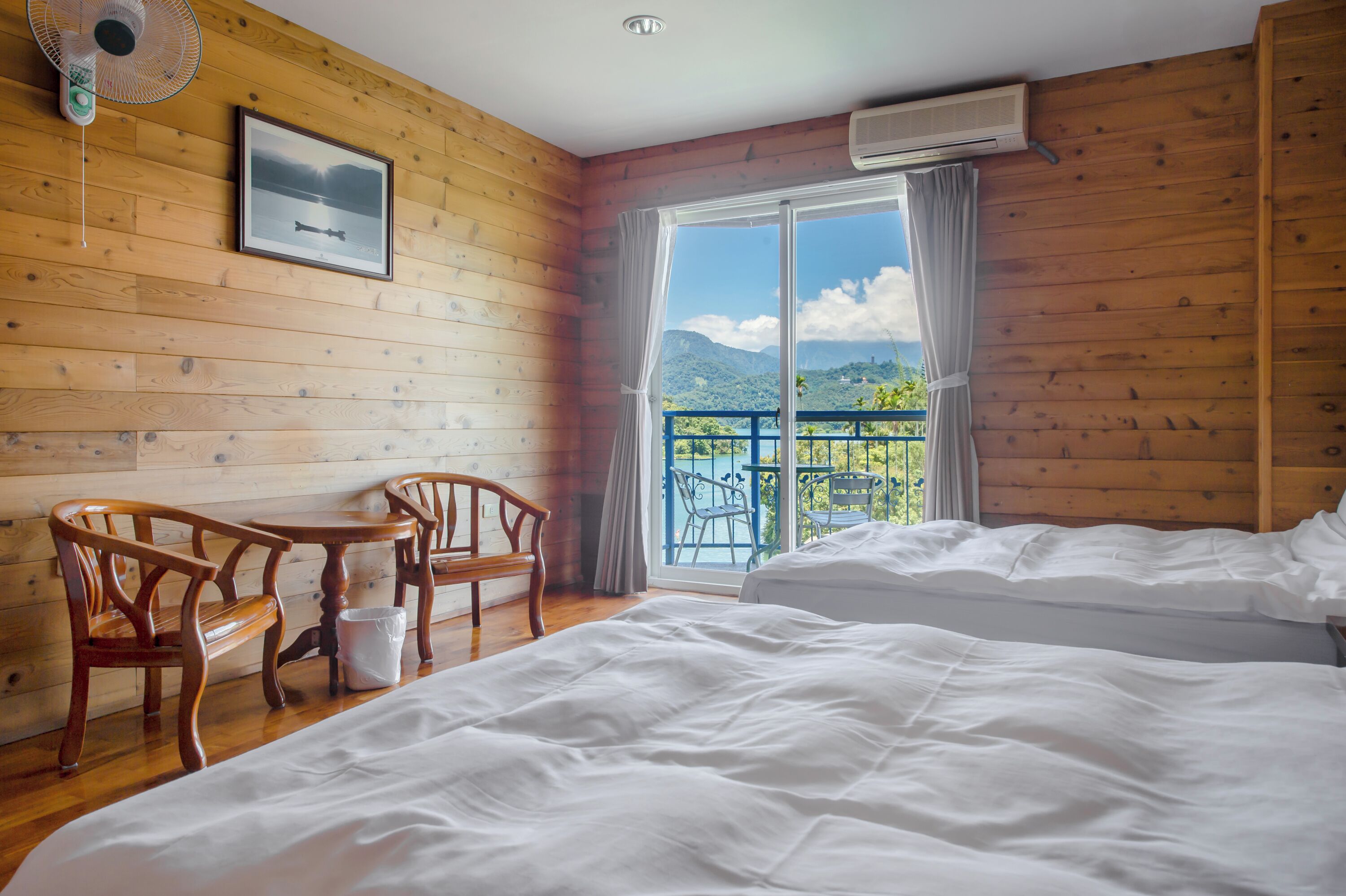 Ein Zimmer mit Holzwänden, einem Bett, zwei Stühlen, einem Tisch und einem Fenster mit Bergblick.