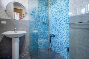 Un baño con lavamanos blanco, cabina de ducha de vidrio y azulejos de mosaico azules en las paredes.