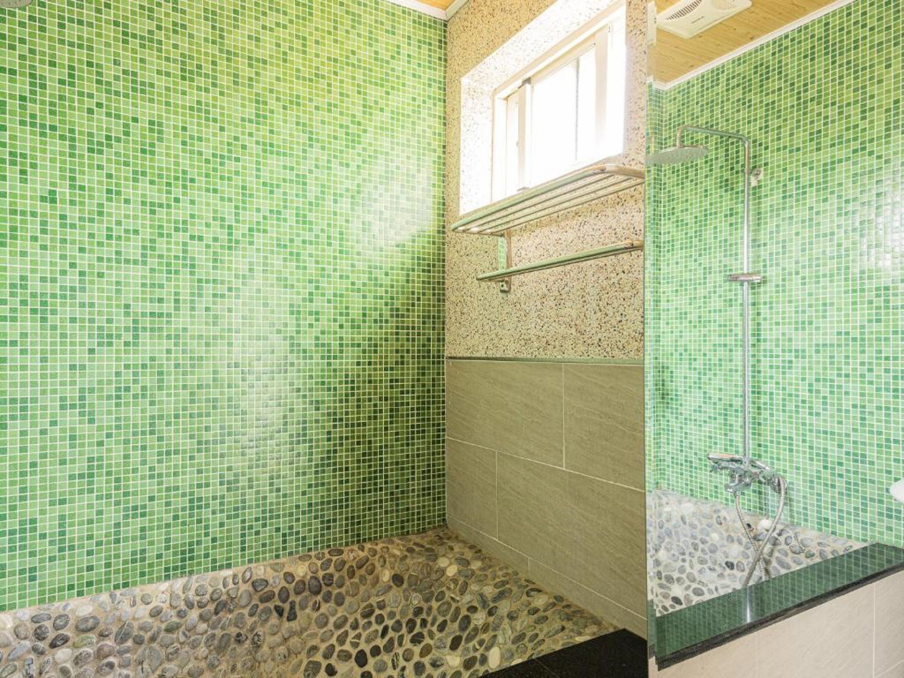 A bathroom with green mosaic tiles, a stone mosaic shower floor, and a glass-enclosed shower area.