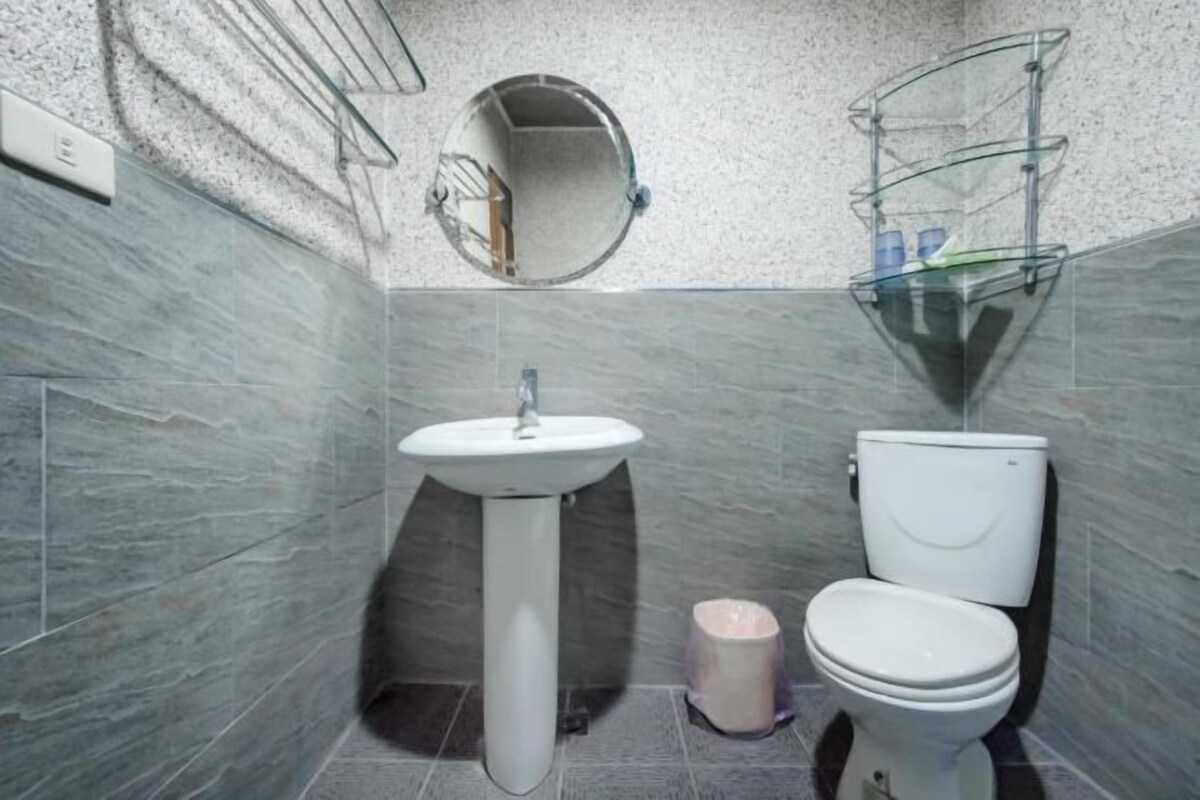 Un baño con lavamanos pedestal, inodoro y espejo redondo.