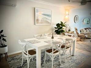 A dining area with a white table and chairs, a large plant, and a painting of a beach scene on the wall. - Stunning, uninterrupted views of beach & surf (Manly)