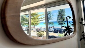 A round mirror reflecting a view of a parking lot with cars and trees, and a clear blue sky. - Stunning, uninterrupted views of beach & surf (Manly)