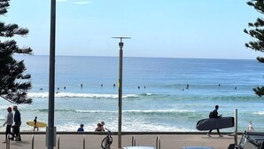 A beach with people walking and surfing, a clear sky, and a calm sea. - Stunning, uninterrupted views of beach & surf (Manly)