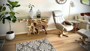A modern living room with a glass coffee table, a leather armchair, a round wooden clock, and a potted plant. - Stunning, uninterrupted views of beach & surf (Manly)