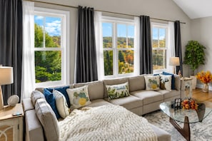 A living room with a sofa, a glass coffee table, and a view of a forest through large windows.
