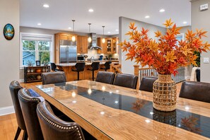 Une cuisine moderne avec un coin repas, comprenant une grande table en bois, des chaises en cuir et un vase décoratif orné de feuilles d ’automne.