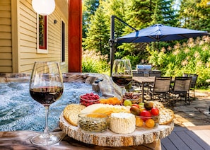 A hot tub with a table set with cheese, crackers, grapes, and wine glasses.