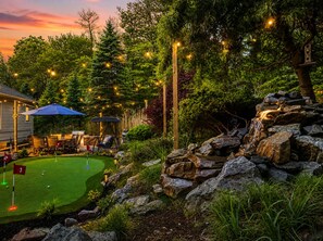 A golf course with a putting green, a swing chair, and a rustic stone wall.