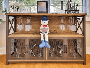 A wooden bar with a bear figure, glassware, and a sign reading 'Cheers'.