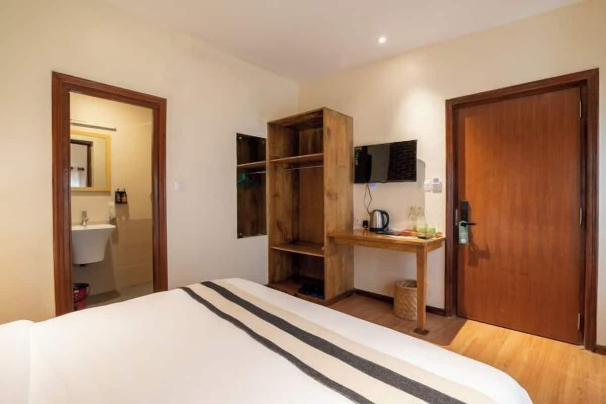 Un dormitorio con cama, armario de madera, escritorio y televisor de pantalla plana, además de una puerta.
