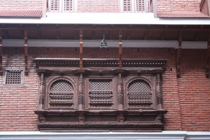 A traditional building with ornate wooden window frames and a balcony. - KGH Patan (Lalitpur)