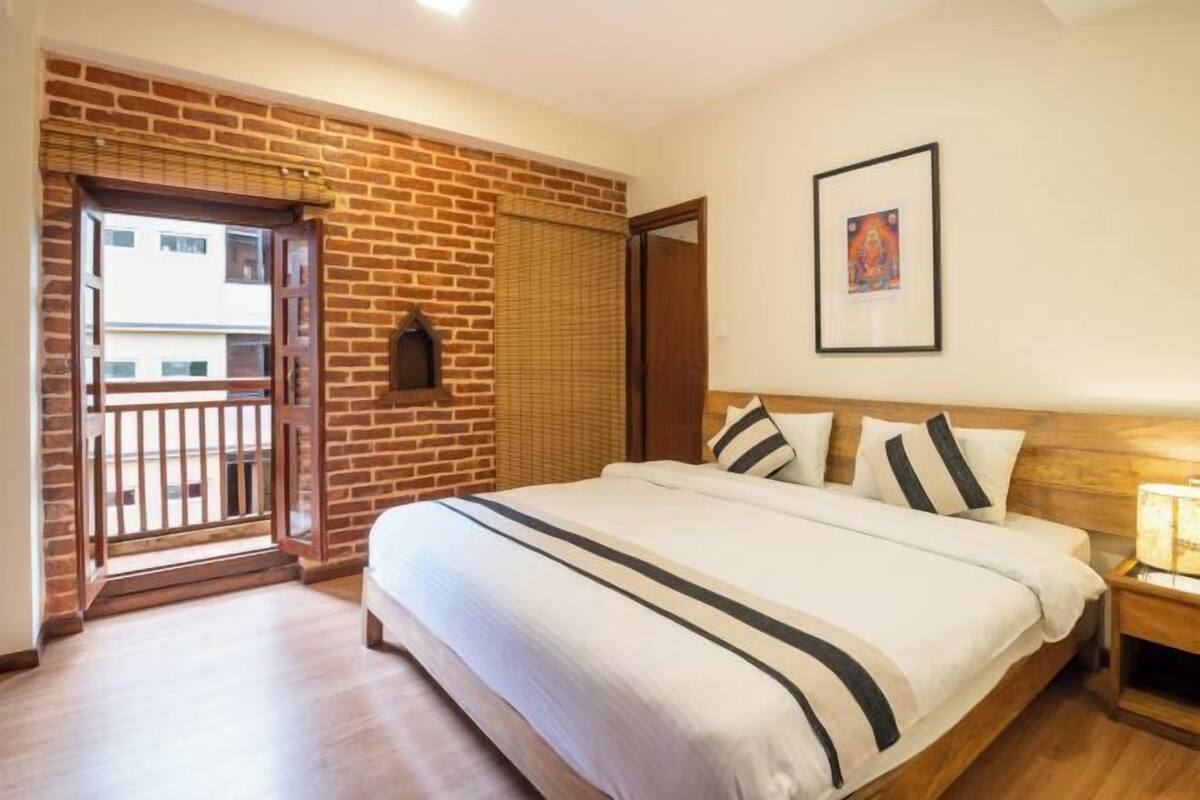 Un dormitorio con pared de ladrillo, una cama con ropa de cama a rayas, un cuadro en la pared y una mesita de noche de madera.