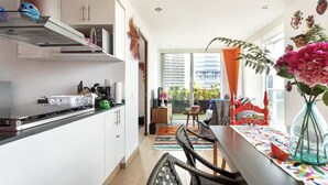 A modern kitchen with white cabinets, a black countertop, and a stainless steel range hood. There is a dining area with a colorful tablecloth, a vase with flowers, and a view of the city through large windows. - Mexican apartment in Polanco. Pool - gym - parking (Ciudad de México)