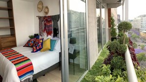 A modern bedroom with a bed, colorful pillows, a striped blanket, and a view of a cityscape through large windows. - Mexican apartment in Polanco. Pool - gym - parking (Ciudad de México)