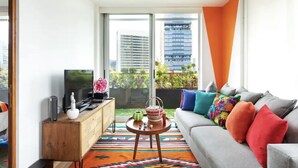 A modern living room with a grey sofa, colorful cushions, a wooden side table, and a television. - Mexican apartment in Polanco. Pool - gym - parking (Ciudad de México)