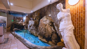 A pool area with a statue, stone walls, and a tiled floor. - Takasago onsen (Asahikawa)