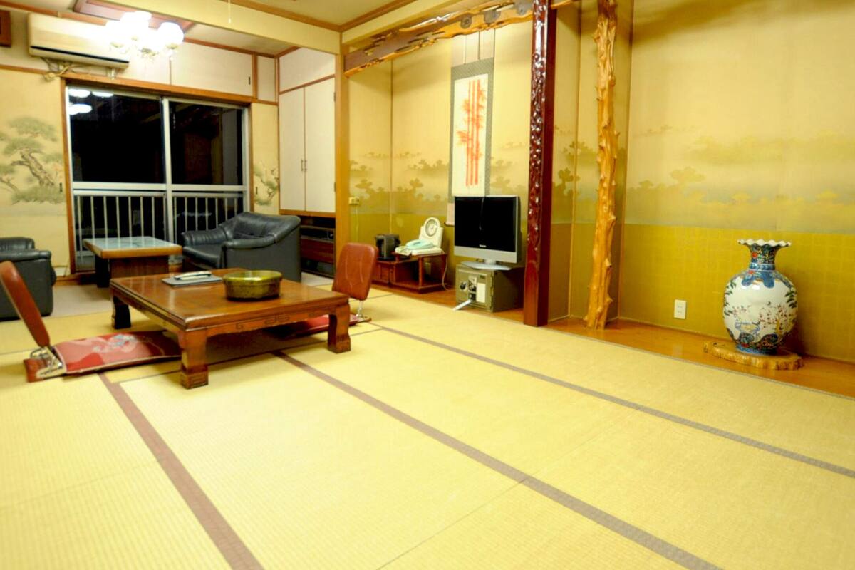 A traditional Japanese room with tatami flooring, a low wooden table, and black leather chairs.