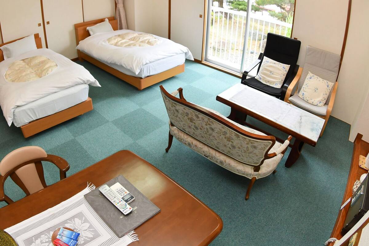 A hotel room with two single beds, a wooden chair, a small table, and a sofa.