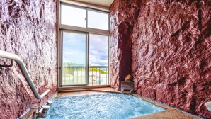 A hot tub with a rocky wall and a large window. - Takasago onsen (Asahikawa)