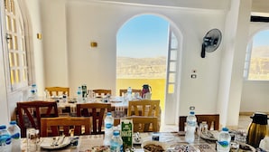 A dining area with tables set for meals, water bottles, and a view of a desert landscape through an open doorway. - Royal Mountain Hotel (Luxor)