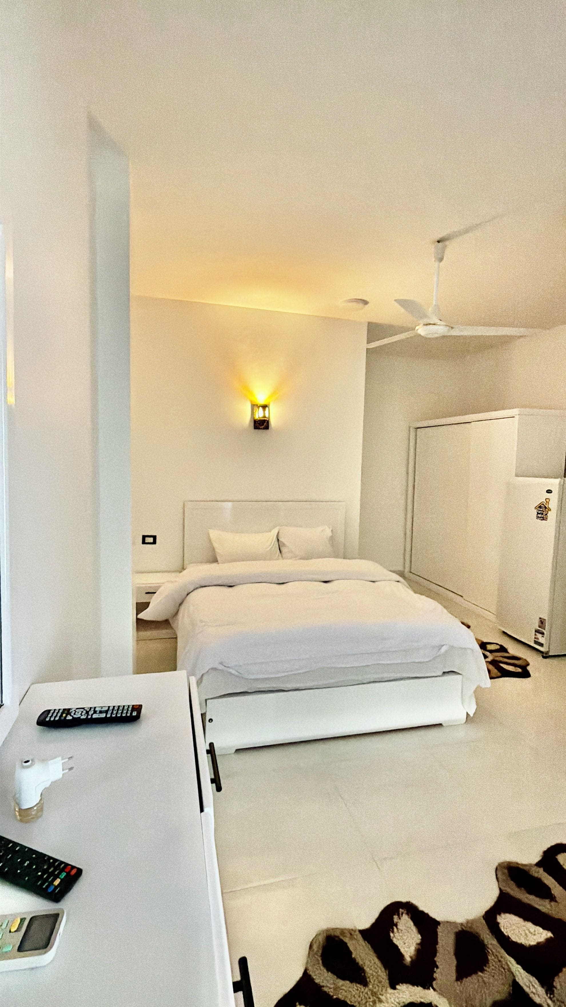 Une chambre d’hôtel équipée d’un lit, d’une table de chevet, d’une télécommande, d’un téléphone portable et d’un luminaire fixé au mur.