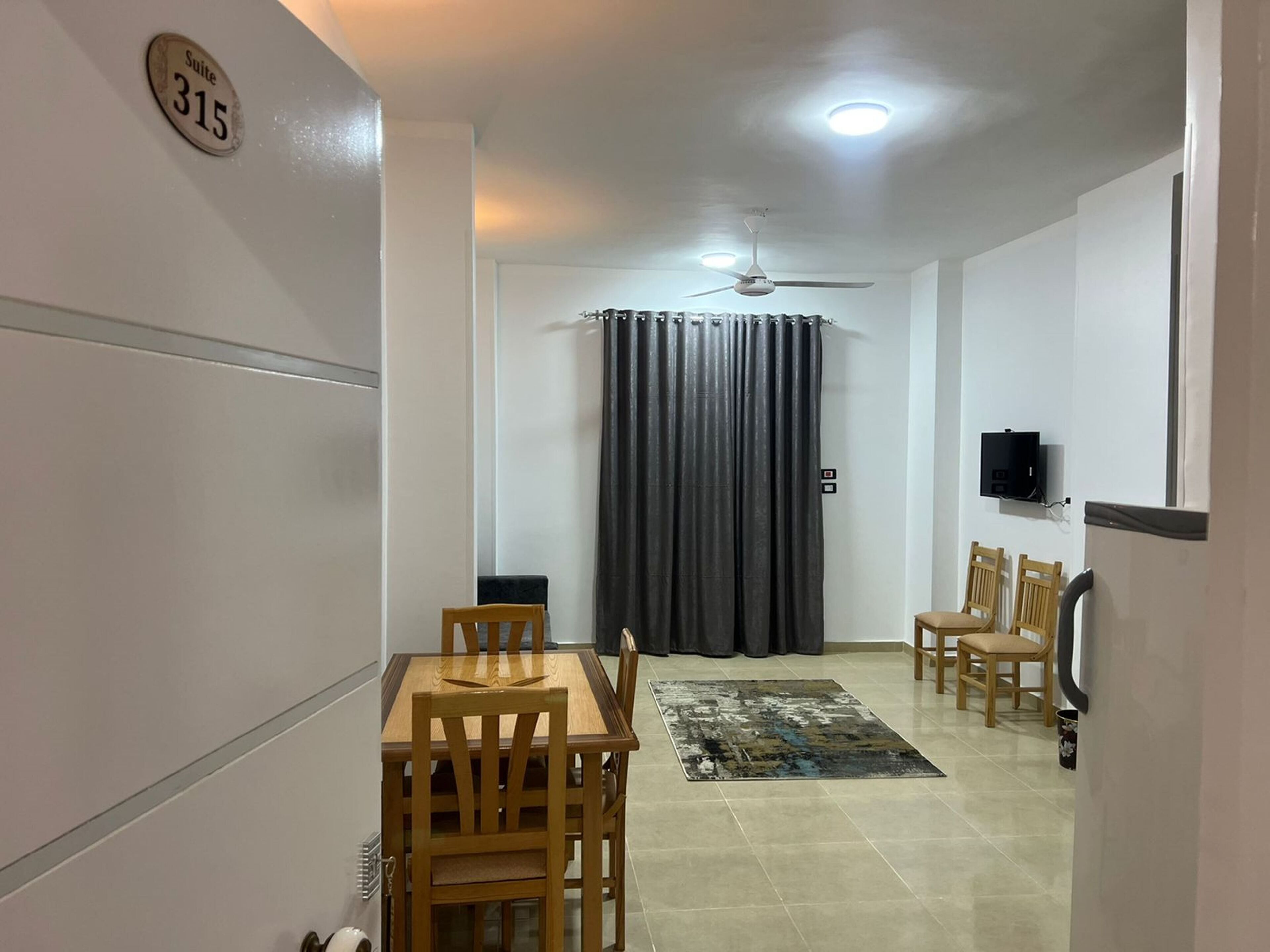 Habitación de hotel con comedor, ventilador de techo, televisor montado en la pared y cortina.