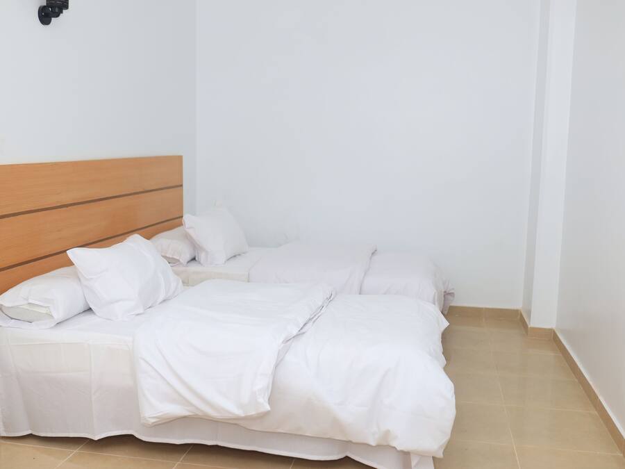 Ein Einzelbett mit Holz-Kopfteil, weißer Bettwäsche und einer schlichten weißen Wand.