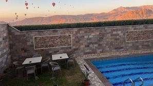 A pool area with stone walls, outdoor seating, and a view of mountains and hot air balloons. - Royal Mountain Hotel (Luxor)