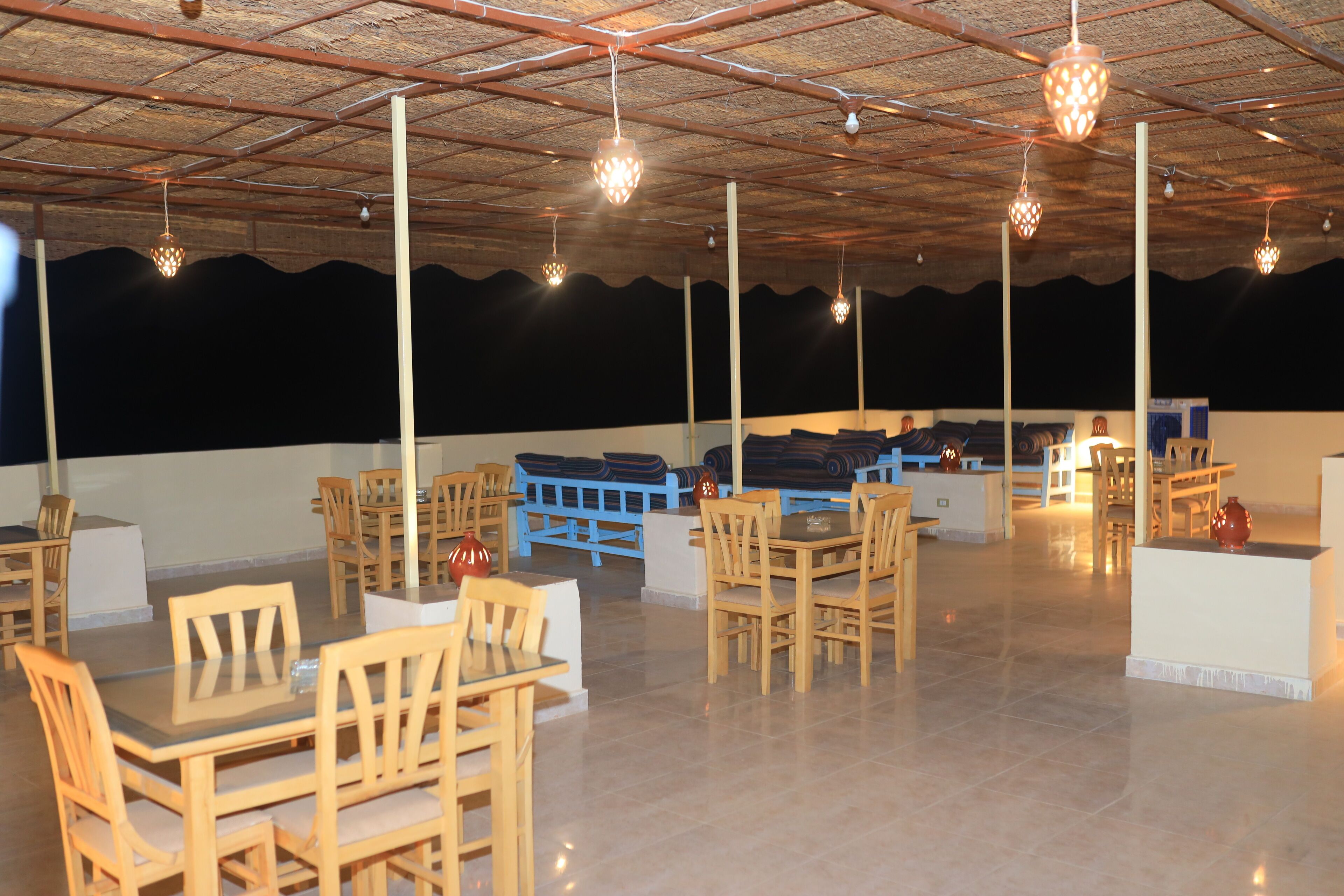 A spacious indoor area with multiple wooden tables and chairs, a high ceiling with exposed beams, and hanging decorative lights.