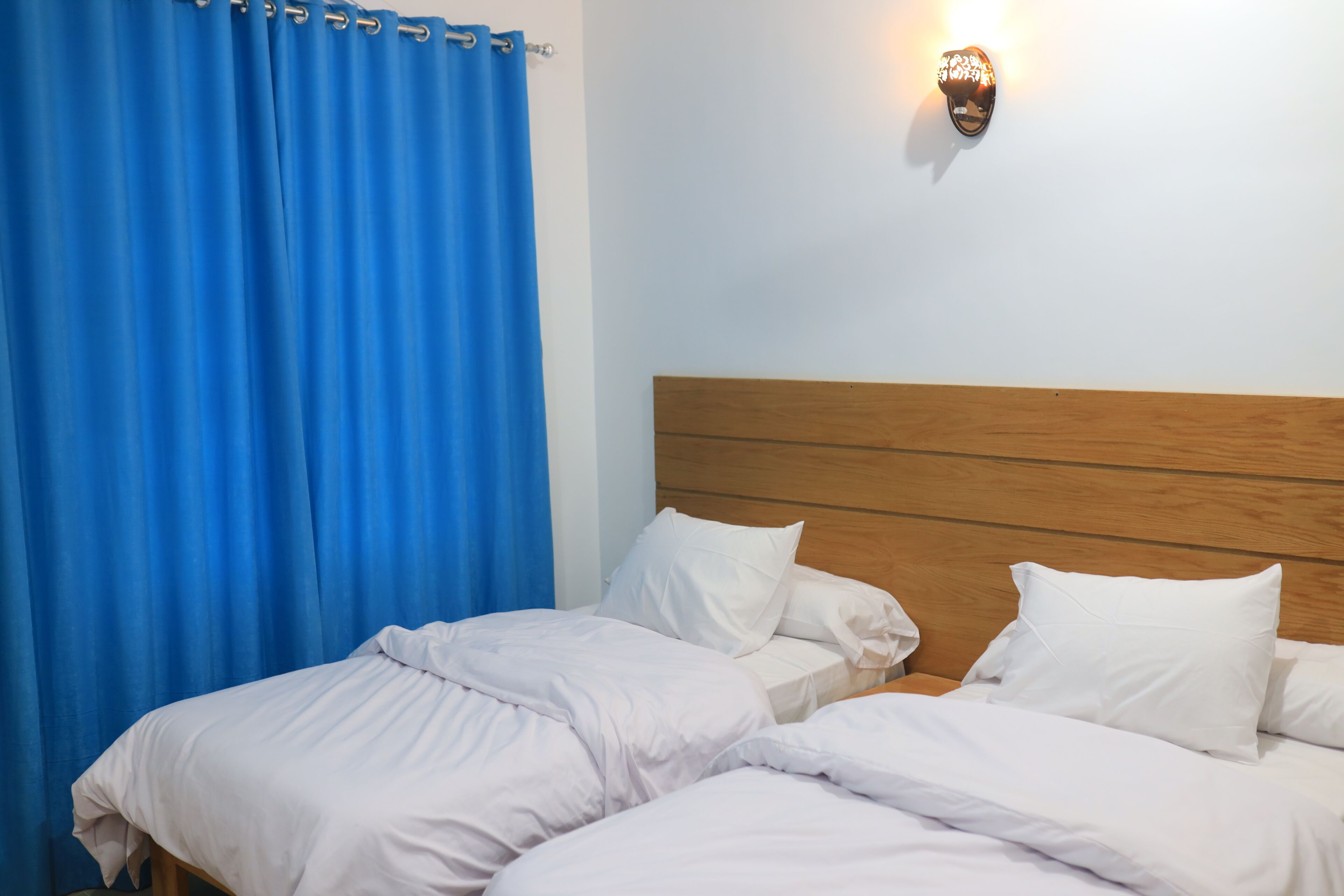 Cama doble con ropa de cama blanca, cabecera de madera y lámpara de pared.