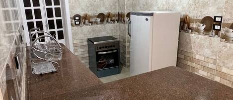 A compact kitchen with a granite countertop, a built-in oven, a refrigerator, and a white door.