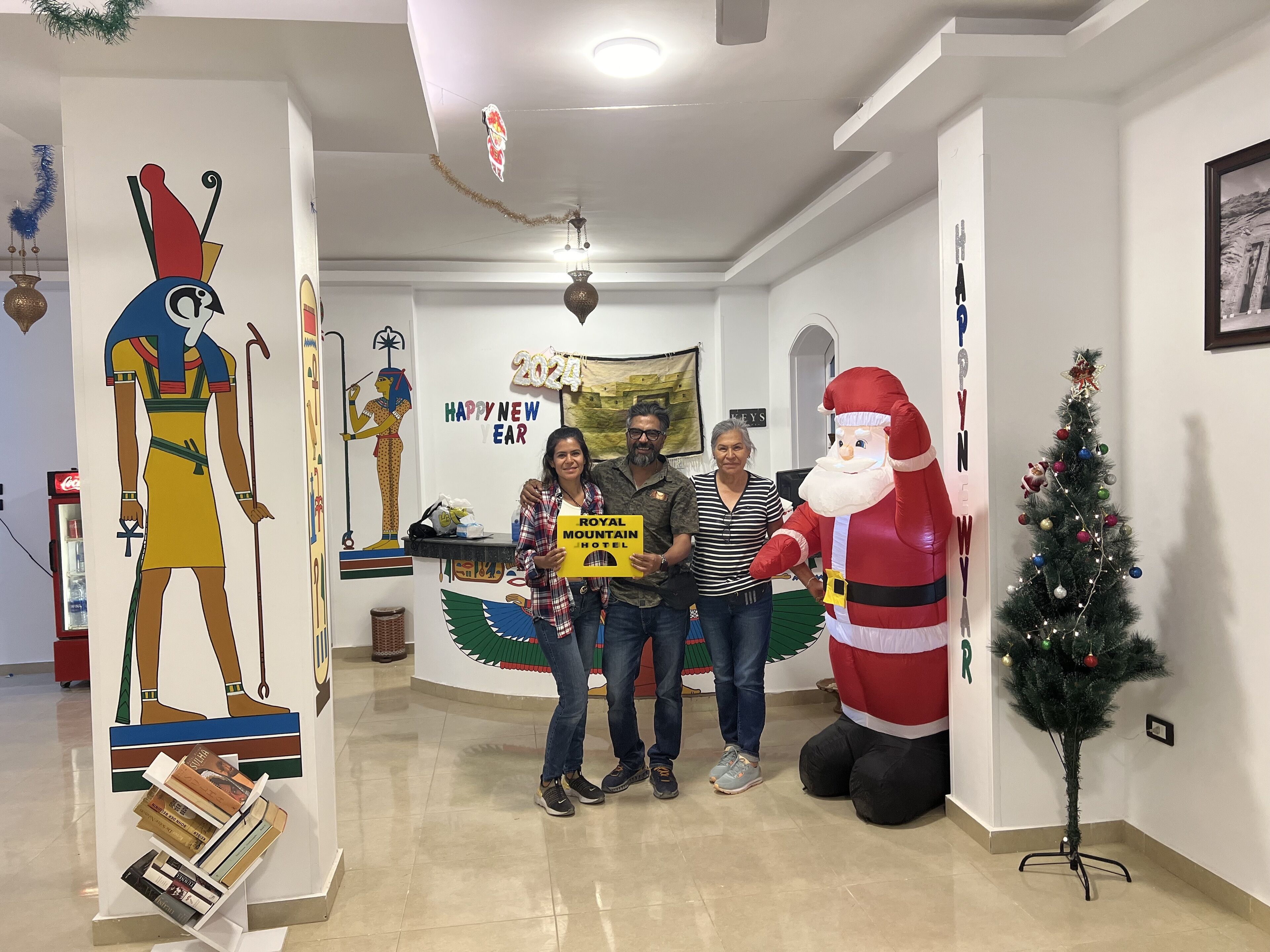 Een hotellobby met een groot Egyptisch beeld, een kerstboom en een spandoek met de tekst 'Happy New Year'.