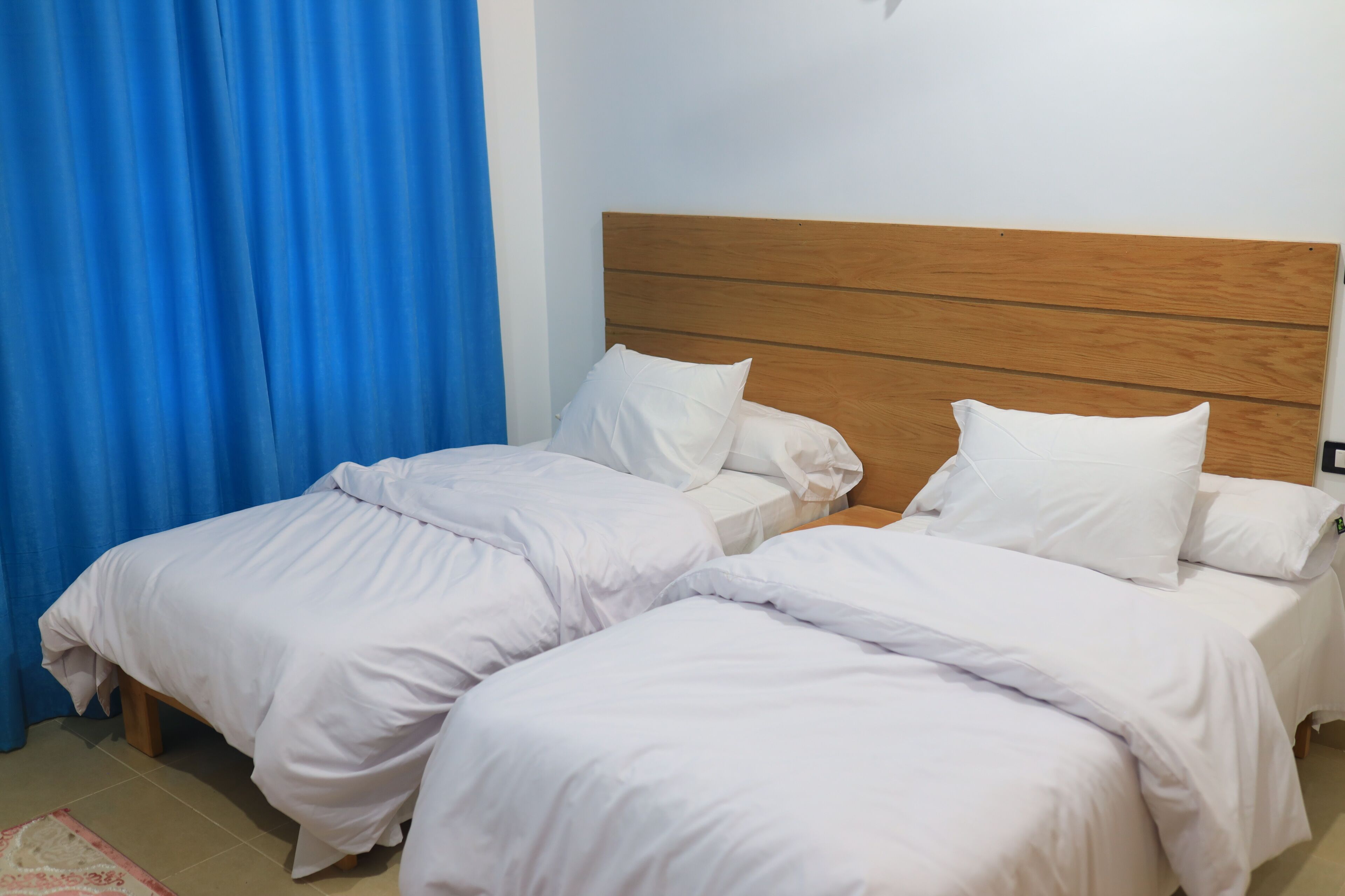 Un dormitorio con dos camas individuales, cabeceros de madera, ropa de cama blanca y una cortina azul.