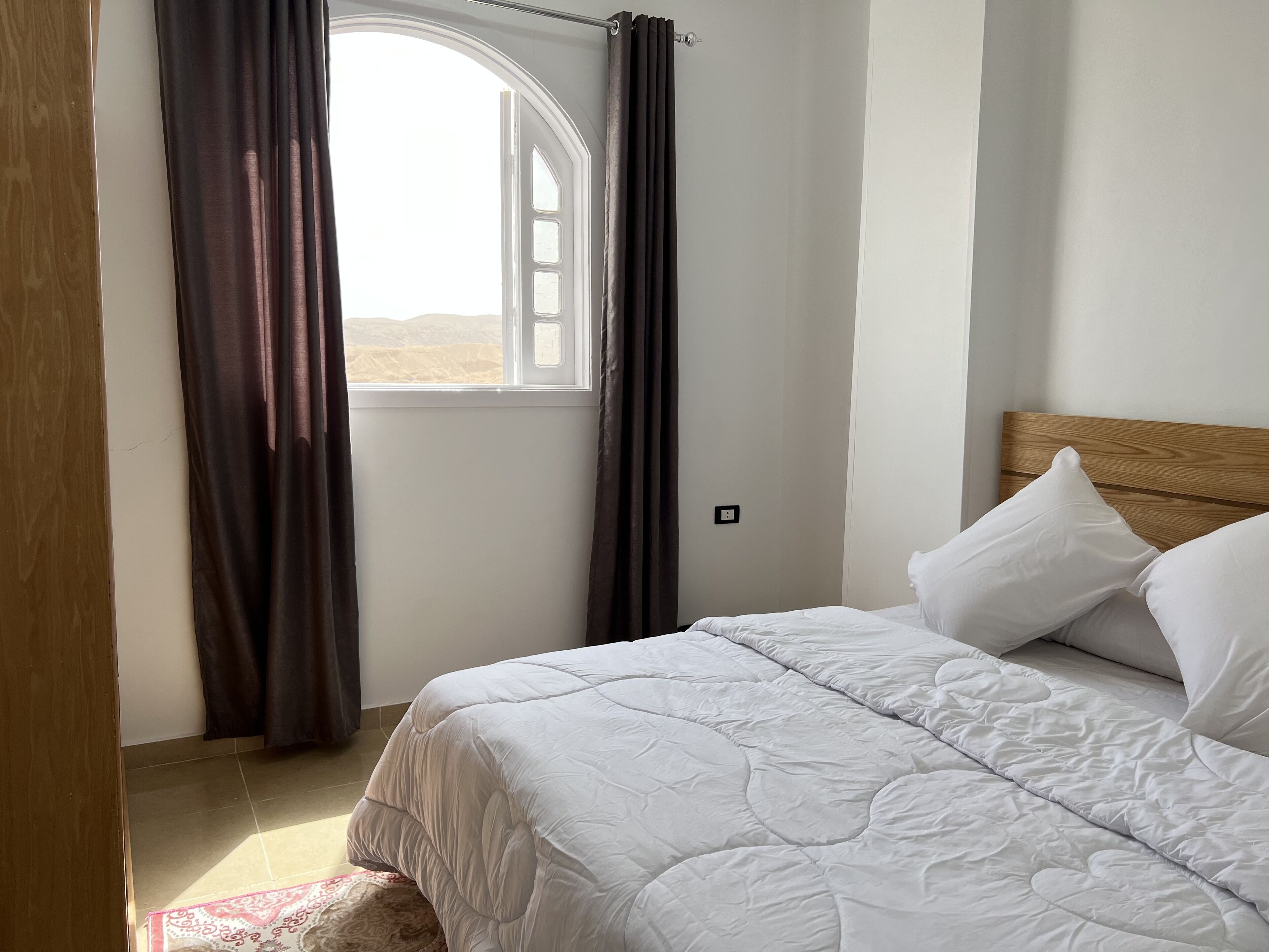 A bedroom with a bed, a window with curtains, and a view of the desert.