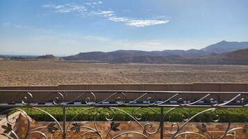 A balcony with a metal railing and decorative elements, overlooking a desert landscape with distant mountains and a clear sky.