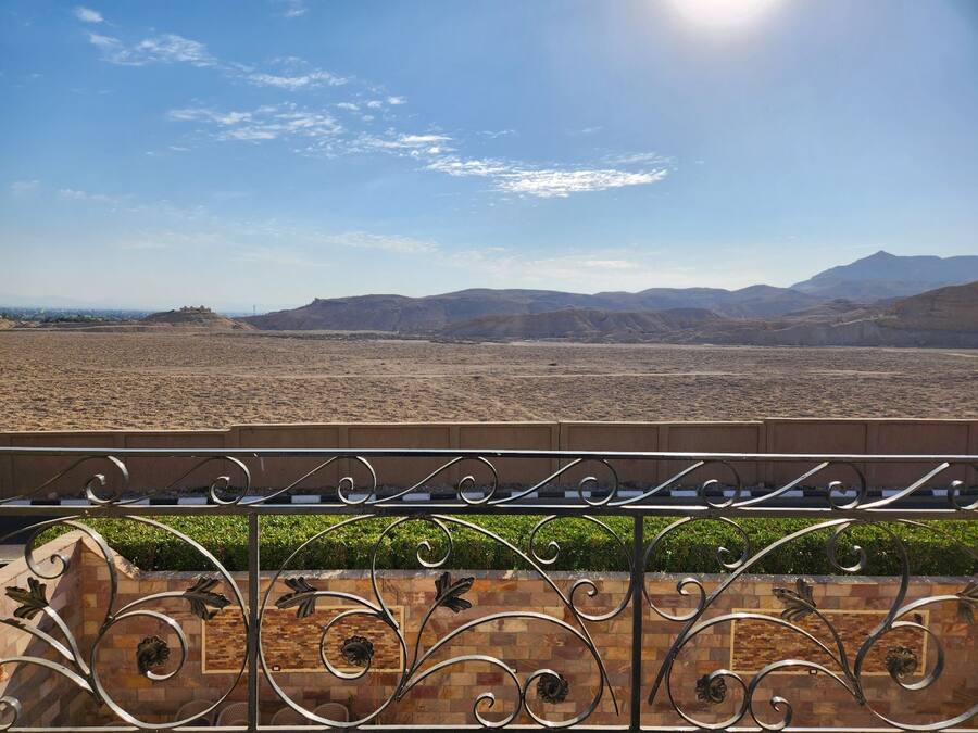 A balcony with a metal railing and decorative elements, overlooking a desert landscape with distant mountains and a clear sky.