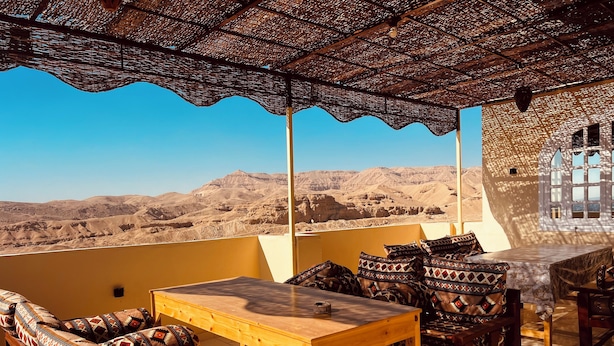 A terrace with wooden furniture, patterned cushions, and a view of desert hills. - Royal Mountain Hotel (Luxor)