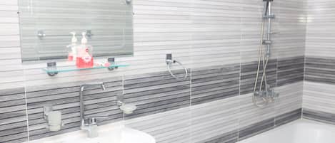 A bathroom with a white sink, a glass shelf with toiletries, a mirror, and a shower.