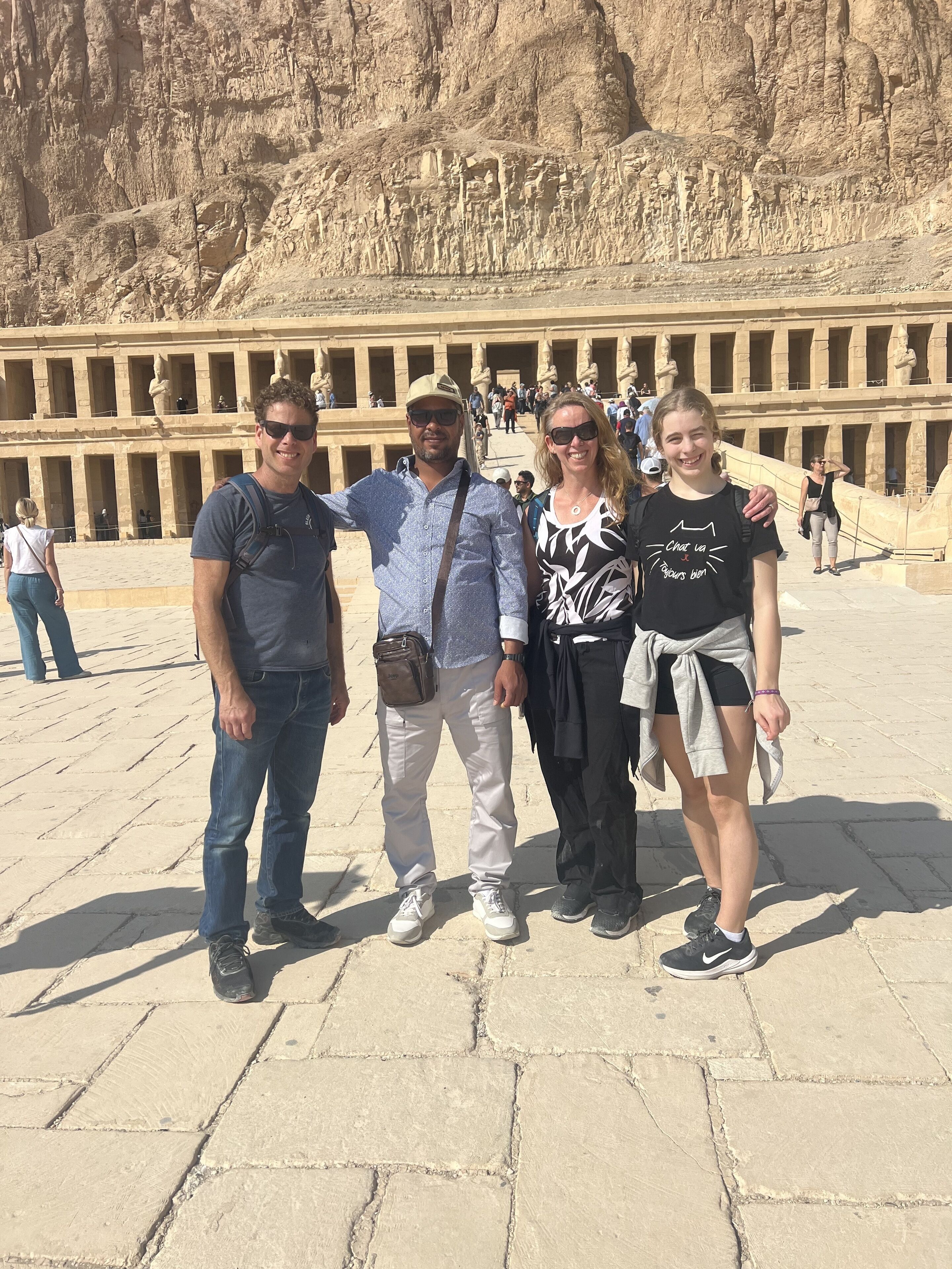 A group of people standing in front of an ancient Egyptian temple with hieroglyphics and statues.