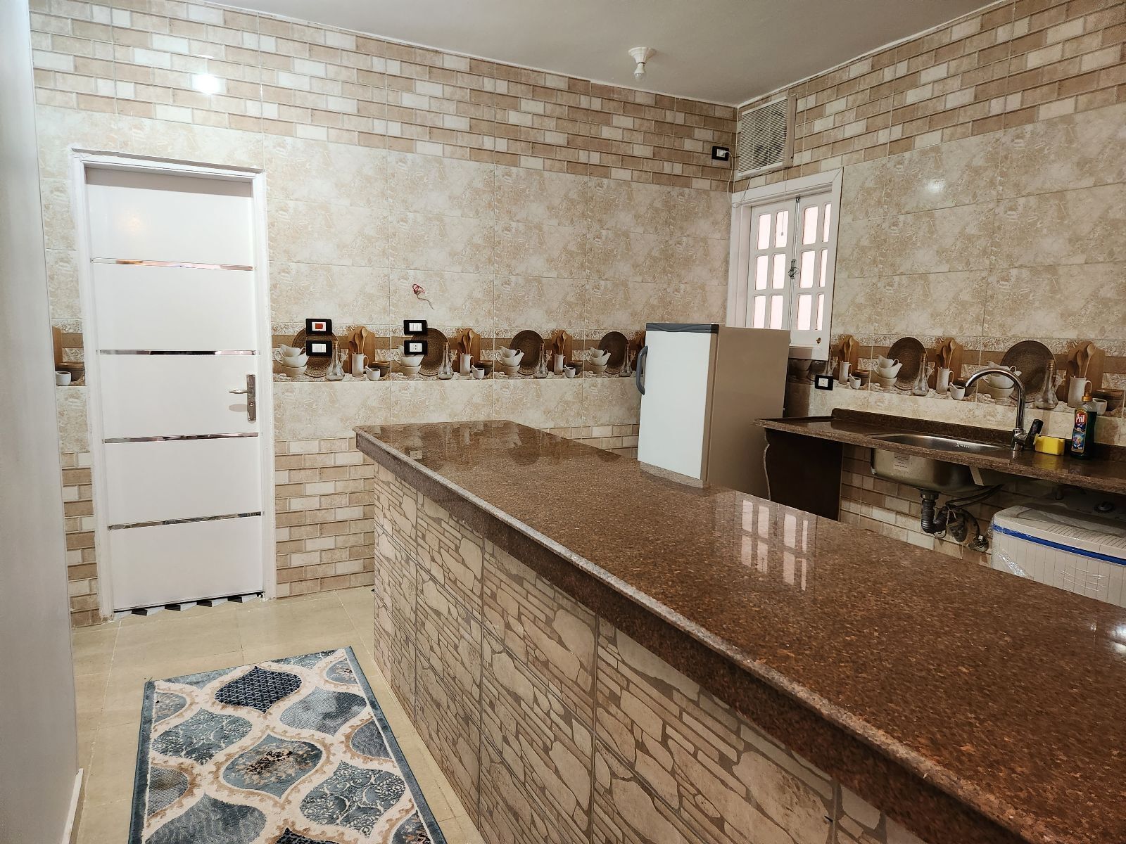 A kitchen with a granite countertop, a built-in sink, and a refrigerator.